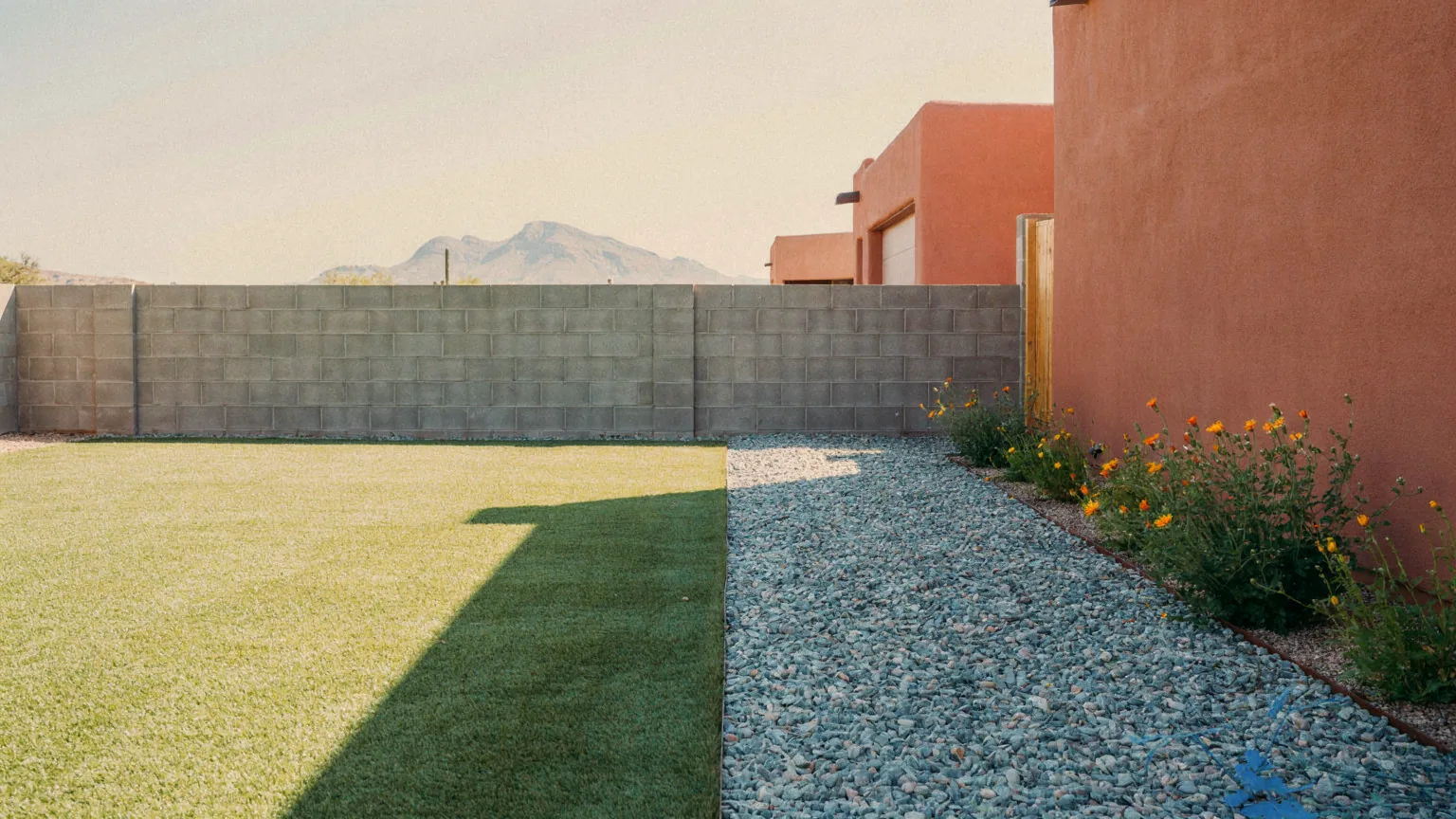 An Albuquerque yard divided between synthetic turf, gravel and desert flowers in strong midday sun.